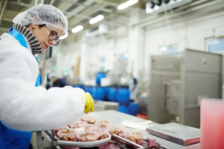 Image of a women wearing overalls, gloves and hair net, working in a food production line.