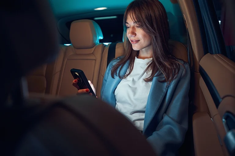 Image of a smartly dressed woman using phone in the back seat of a car at night